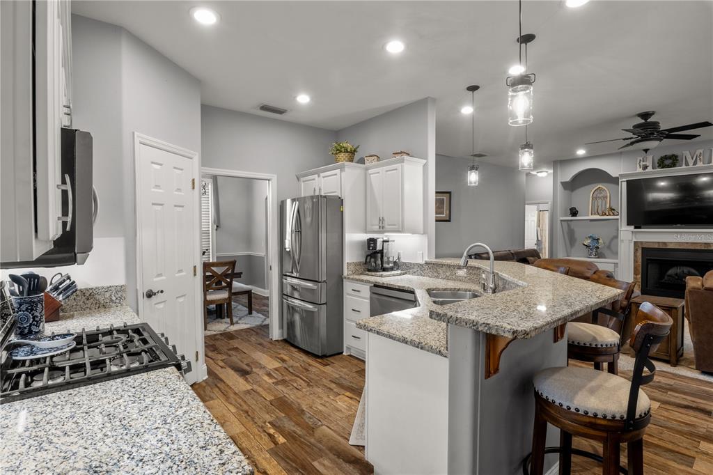 A kitchen features granite countertops, stainless steel appliances, white cabinetry, and wood-look flooring — 651 HART LAKE DRIVE, WINTER HAVEN, FL