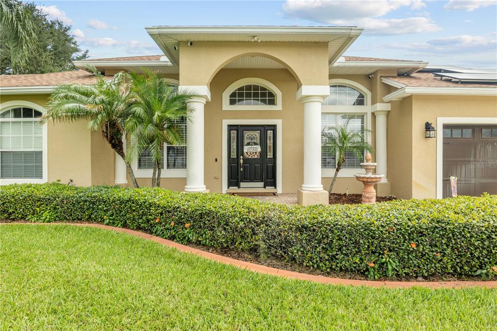 The exterior of a tan house features a covered entryway with white columns and landscaping — 651 HART LAKE DRIVE, WINTER HAVEN, FL