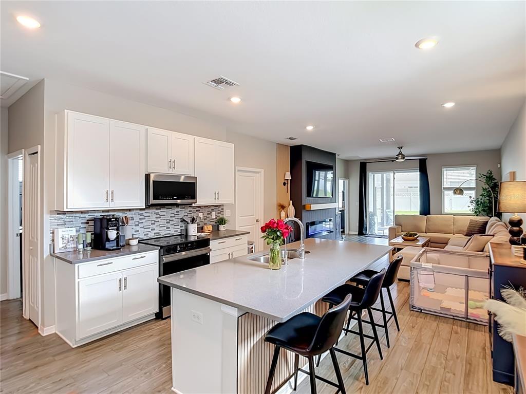 A modern kitchen with white cabinets, a large island, and an open-concept living area — 7531 ASHCROFT DRIVE, WESLEY CHAPEL, FL