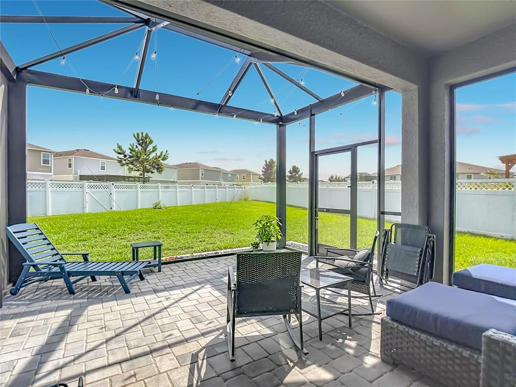 A screened-in patio features paver flooring, outdoor furniture, and a view of a fenced backyard — 7531 ASHCROFT DRIVE, WESLEY CHAPEL, FL