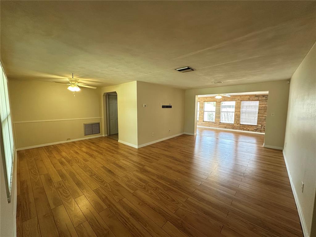 An open-concept living area features light wood-look flooring, a ceiling fan, and a sunroom beyond — 3313 BRIAR CLIFF DRIVE, HOLIDAY, FL