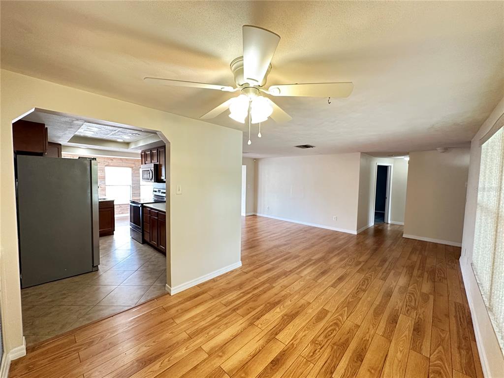 A living room with wood-look flooring and a ceiling fan opens into a tiled kitchen — 3313 BRIAR CLIFF DRIVE, HOLIDAY, FL