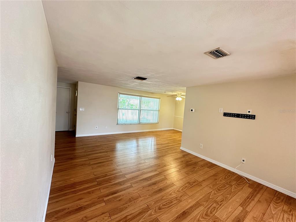 An empty living room features light-colored walls, wood-look flooring, and a large window with blinds — 3313 BRIAR CLIFF DRIVE, HOLIDAY, FL