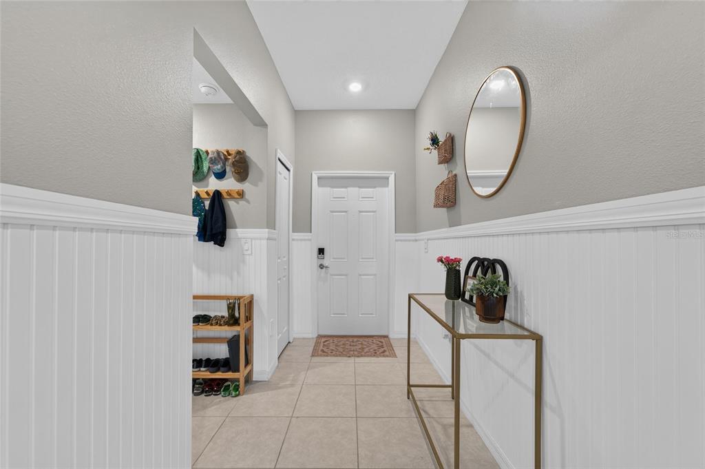 An entryway features white beadboard wainscoting, a console table, a wall mirror, and a shoe rack — 4450 COZY CONDOR COURT, BARTOW, FL