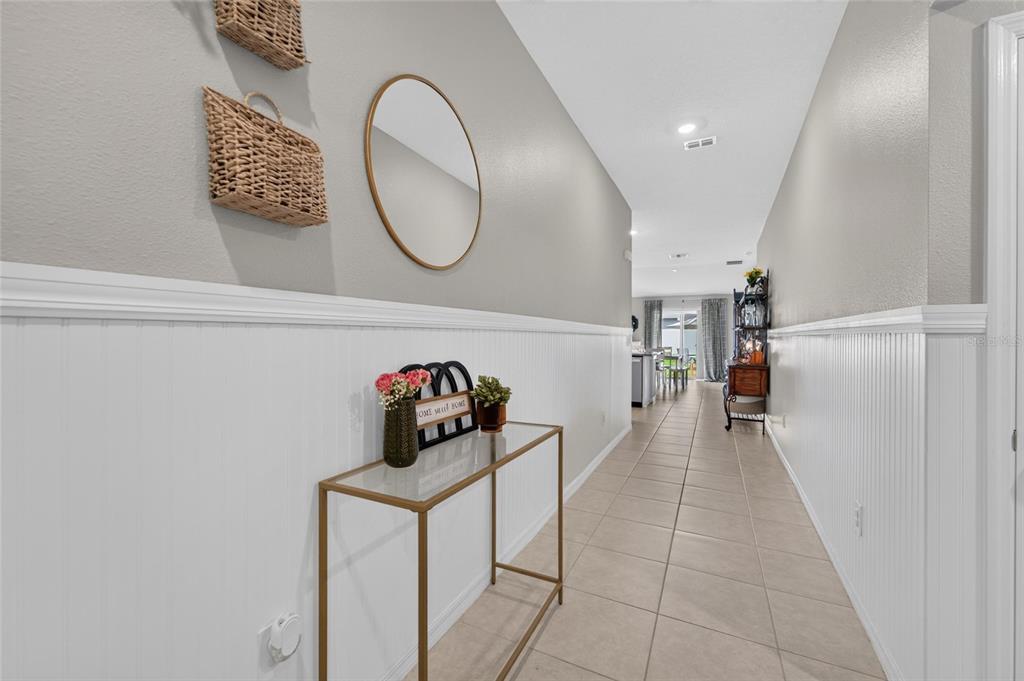 A hallway features white wainscoting, a gold console table, a round mirror, and woven baskets — 4450 COZY CONDOR COURT, BARTOW, FL