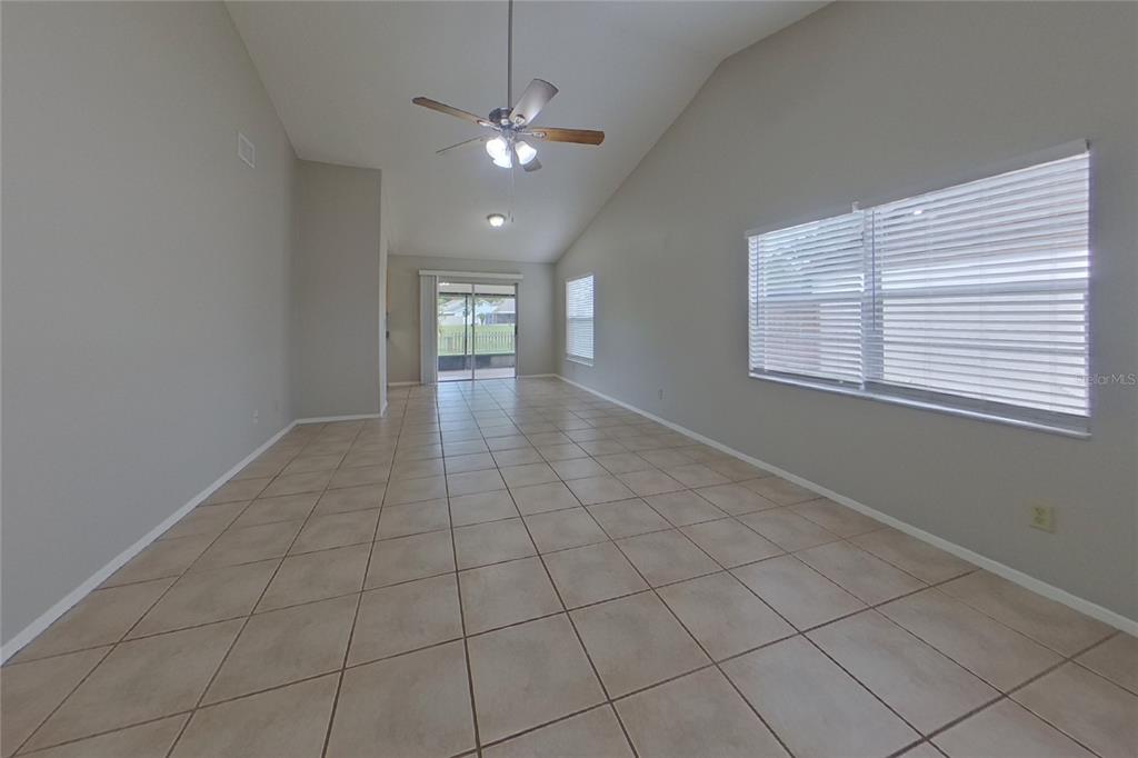 An empty living room features beige tile flooring, vaulted ceilings, and large windows with blinds — 13311 LARAWAY DRIVE, RIVERVIEW, FL