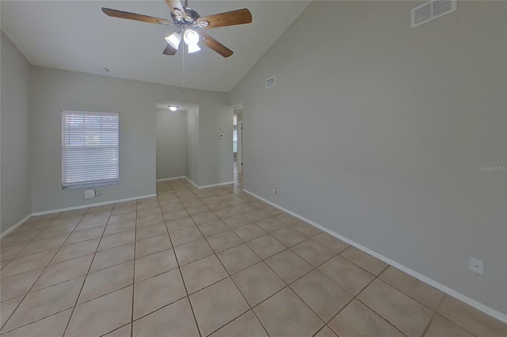 An empty room features light-colored tile flooring, gray walls, and a vaulted ceiling with a fan — 13311 LARAWAY DRIVE, RIVERVIEW, FL