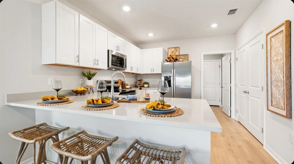 A modern kitchen features white cabinets, stainless steel appliances, and a quartz breakfast bar island — 6565 EQUINOX LANE, NORTH FORT MYERS, FL