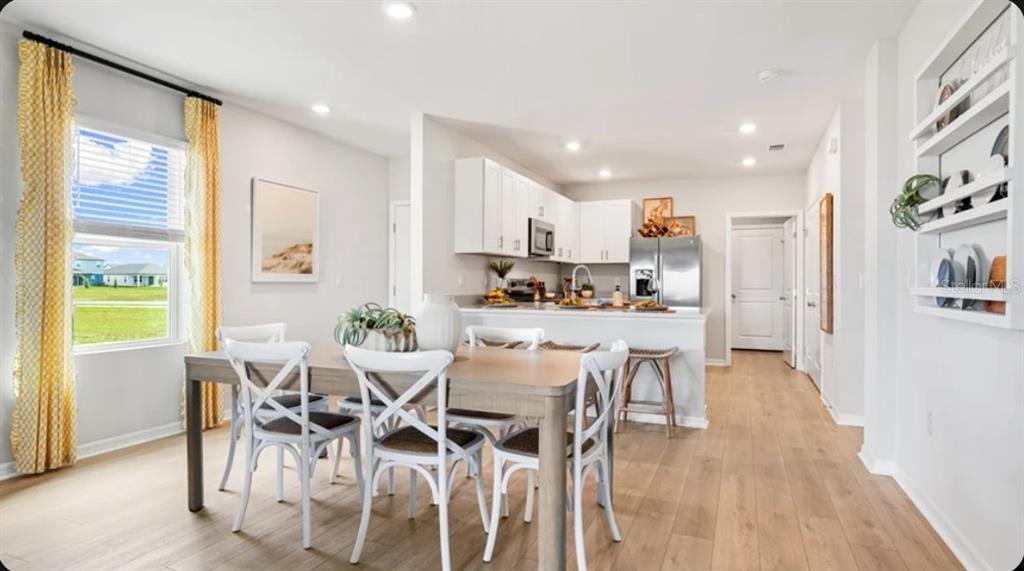 A dining area with a wooden table and white chairs sits before an open kitchen — 6565 EQUINOX LANE, NORTH FORT MYERS, FL