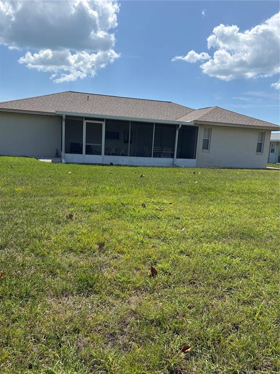 The rear exterior of a house features a screened-in patio and a large grassy yard — 157 ANNAPOLIS LANE, ROTONDA WEST, FL