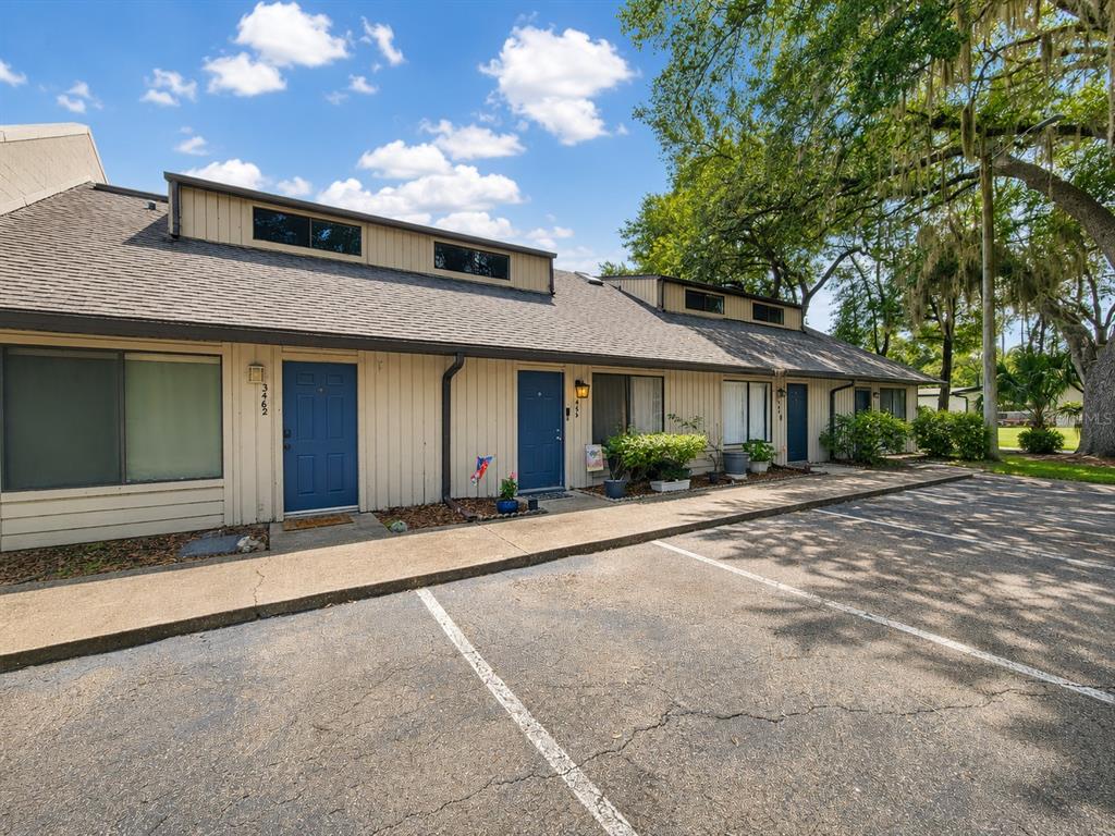 A row of single-story townhomes with blue doors and beige siding faces a parking lot — 3464 NW 37TH AVENUE, GAINESVILLE, FL