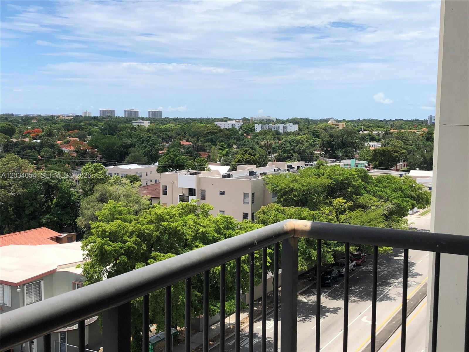 A view from a balcony overlooking a street, trees, and residential buildings under a cloudy sky — 1690 SW 27th Ave # 803, Miami FL 33145, MIAMI, FL