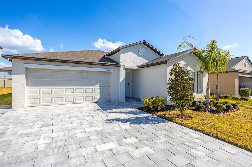 A single-story house with a white stucco exterior, a garage, and palm trees in front — 15415 MILLER CREEK DRIVE, SUN CITY CENTER, FL