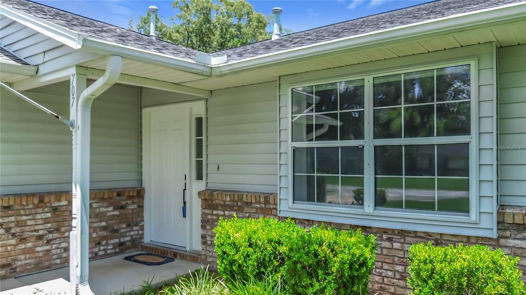The exterior of a house features light green siding, brick accents, and a white front door — 707 NE 46TH COURT, OCALA, FL