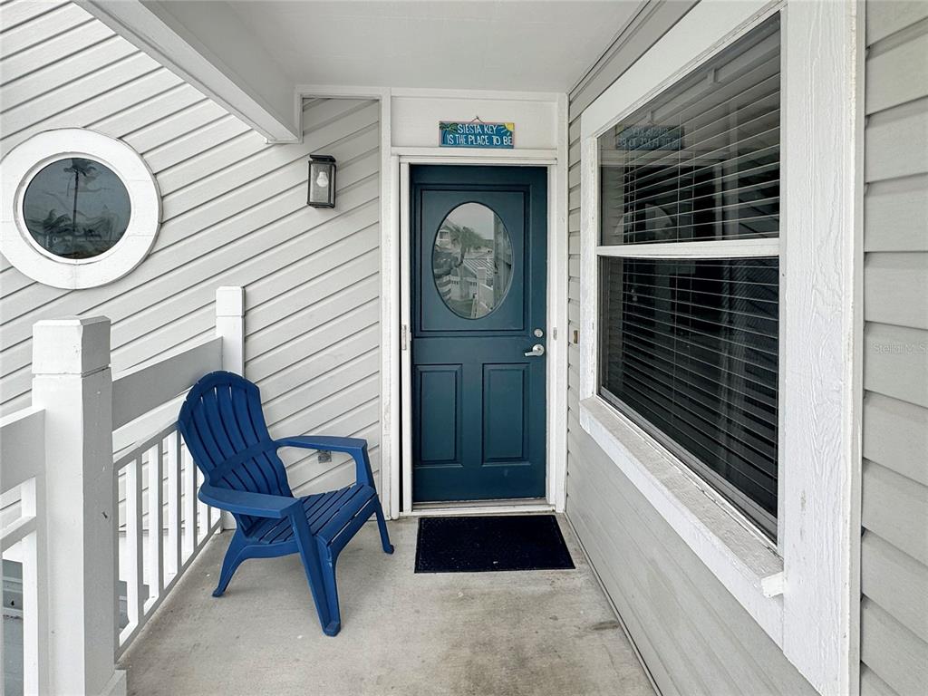 A blue Adirondack chair sits on a covered porch next to a blue front door — 1350 SIESTA BAYSIDE DRIVE UNIT 1350-B, SARASOTA, FL