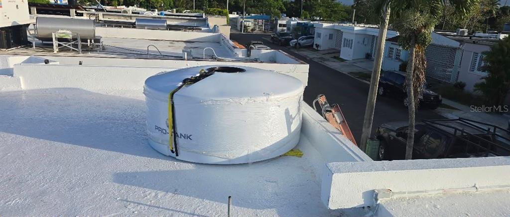 A white water tank sits on a flat, white-painted rooftop next to a ladder — 210 CALLE FIRMAMENTO, CAROLINA, PR