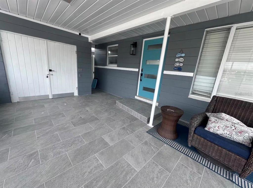 A covered patio features gray tile flooring, a teal front door, and a wicker chair — 1473 DURLING DRIVE S, SOUTH PASADENA, FL
