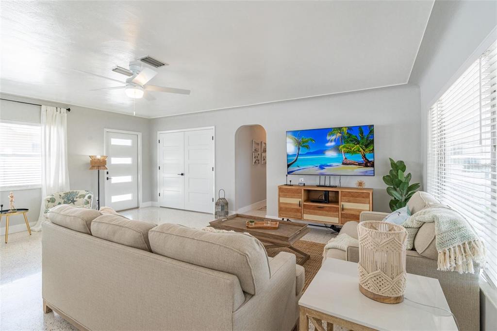A bright living room features a beige sofa, a wooden coffee table, and a wall-mounted television — 1473 DURLING DRIVE S, SOUTH PASADENA, FL