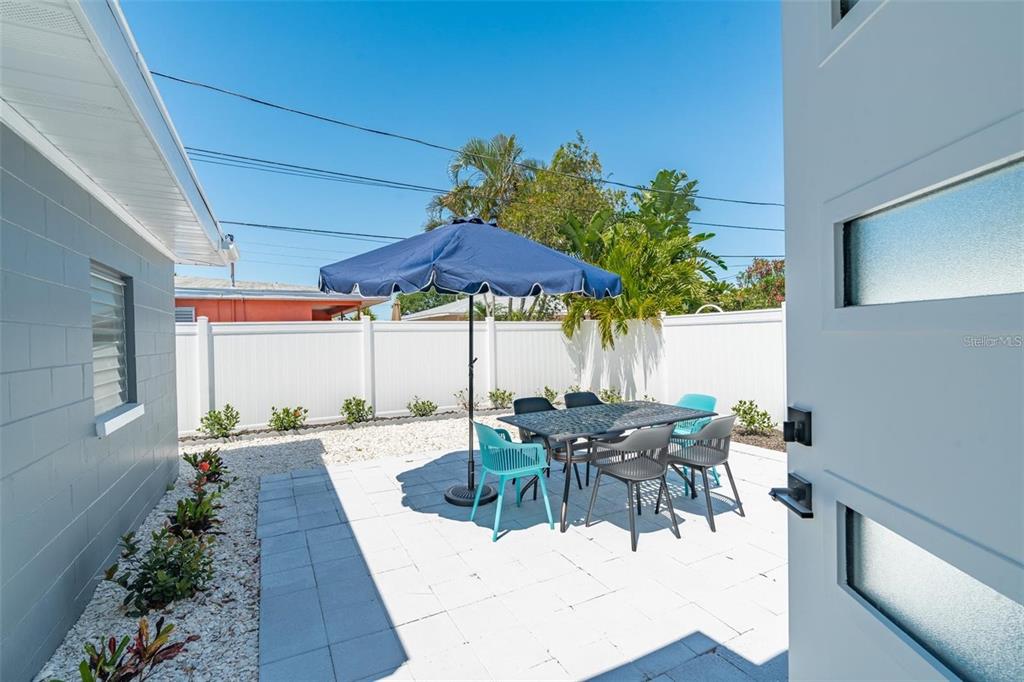 A patio with a dining set and umbrella sits beside a house with white fencing — 1473 DURLING DRIVE S, SOUTH PASADENA, FL