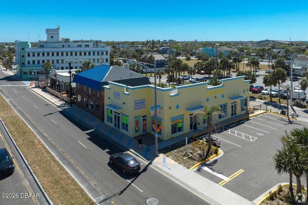 An aerial view shows a yellow commercial building with a parking lot and surrounding streets — 128 S ATLANTIC AVENUE, DAYTONA BEACH, FL