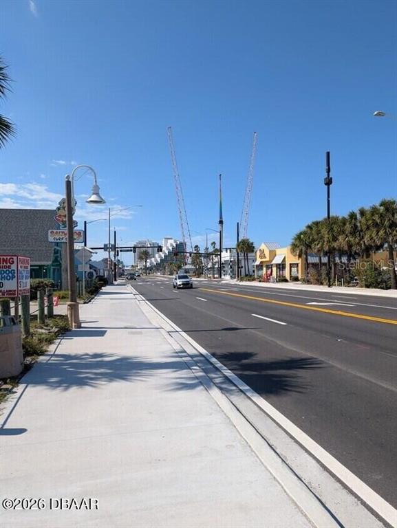 A sidewalk runs alongside a multi-lane road with construction cranes visible in the distance — 128 S ATLANTIC AVENUE, DAYTONA BEACH, FL