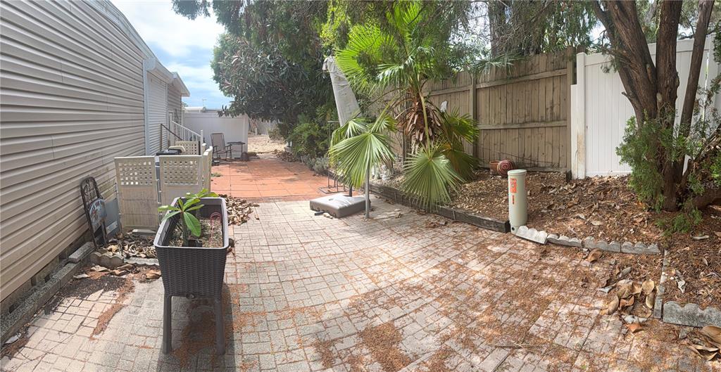 A paved backyard patio features a planter, a palm tree, and a wooden privacy fence — 3301 ALT 19 UNIT 130, DUNEDIN, FL