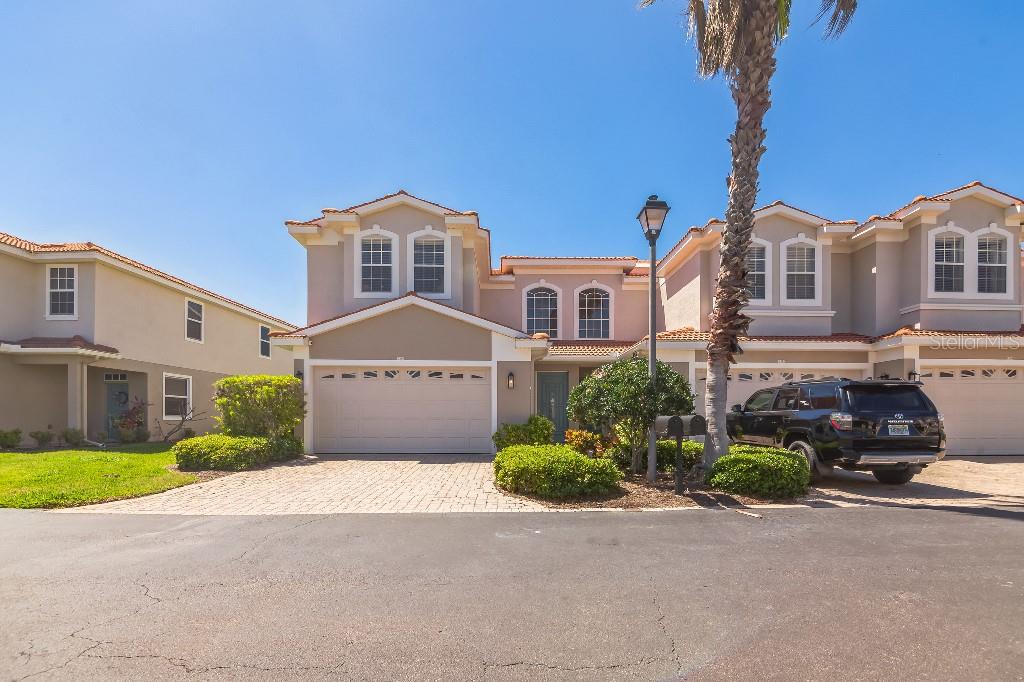 A two-story townhouse with a beige stucco exterior, a two-car garage, and a paved driveway — 1340 RIBOLLA DRIVE, PALM HARBOR, FL