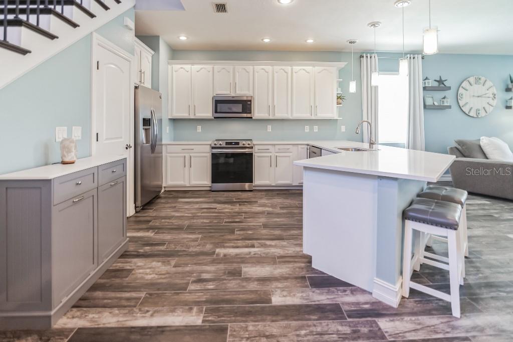 A kitchen with white cabinets, stainless steel appliances, a gray island, and wood-look tile flooring — 1340 RIBOLLA DRIVE, PALM HARBOR, FL