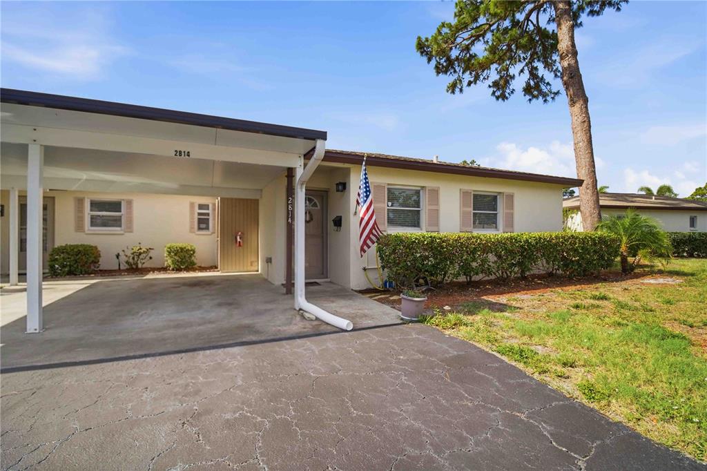 A single-story house features a carport, a front door with an American flag, and landscaping — 2814 SWIFTON DRIVE UNIT 108, SARASOTA, FL