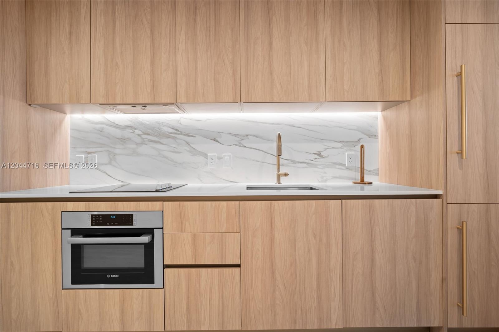 A modern kitchen features light wood cabinetry, a marble backsplash, and stainless steel appliances — 77 SE 5 Street # 2313, Miami FL 33131, MIAMI, FL