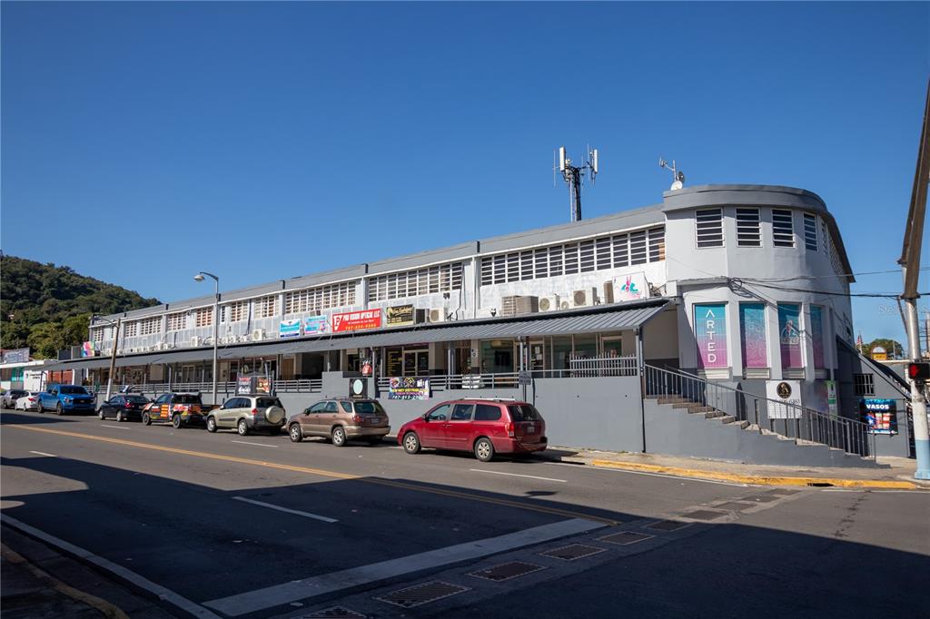 A multi-story commercial building with a curved corner, storefronts, and parked cars along the street — Ave Castro Perez, SAN GERMAN, SAN GERMAN, PR