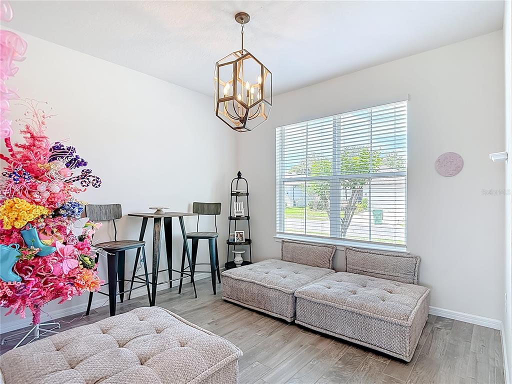 A dining room features a wooden table, upholstered chairs, a geometric chandelier, and a window — 6136 BRADFORD WOODS DRIVE, ZEPHYRHILLS, FL