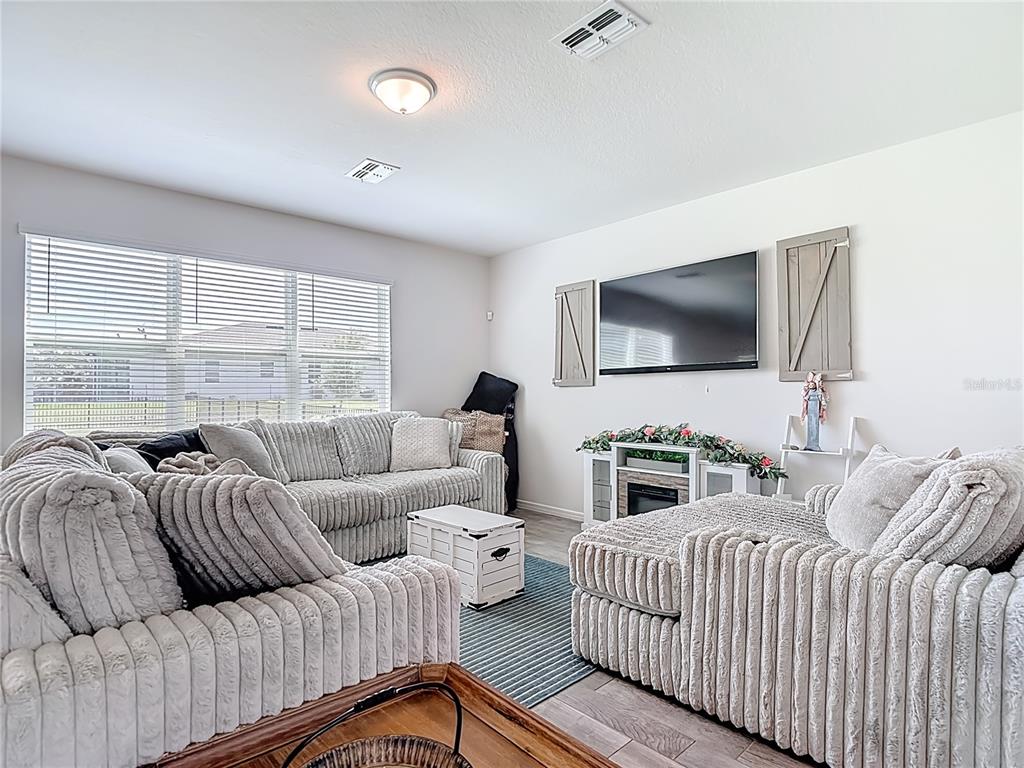 A living room features a textured sectional sofa, a wall-mounted television, and wood-look flooring — 6136 BRADFORD WOODS DRIVE, ZEPHYRHILLS, FL