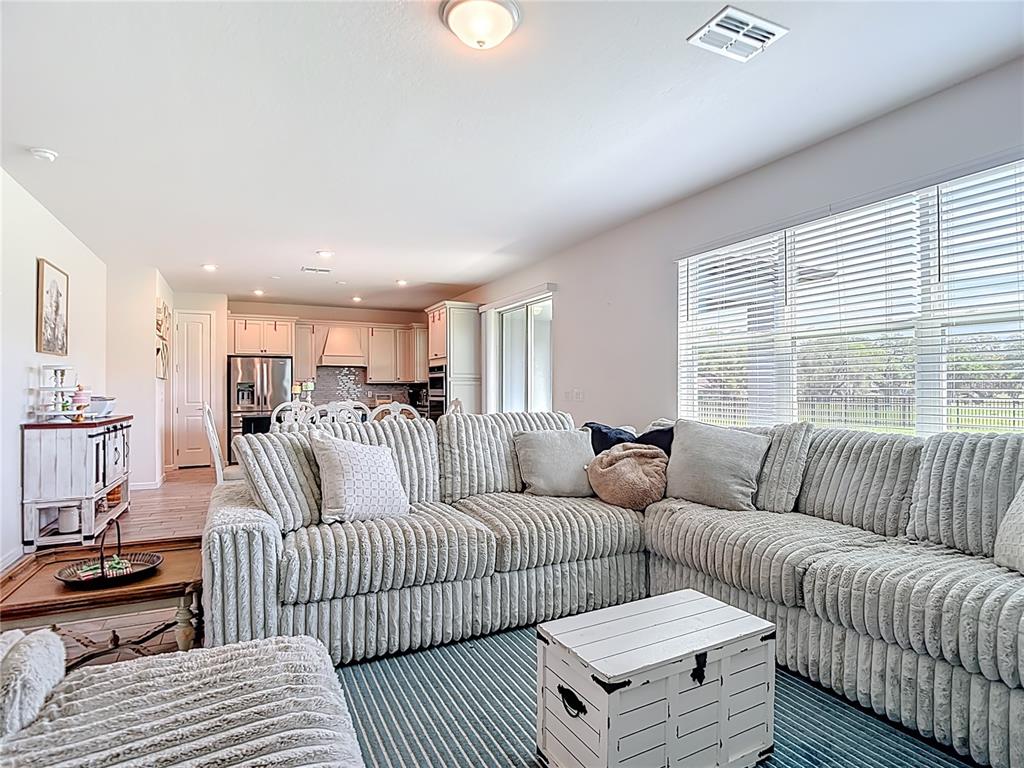 A virtually staged living room features a sofa, coffee table, fireplace console, and wall-mounted television — 6136 BRADFORD WOODS DRIVE, ZEPHYRHILLS, FL