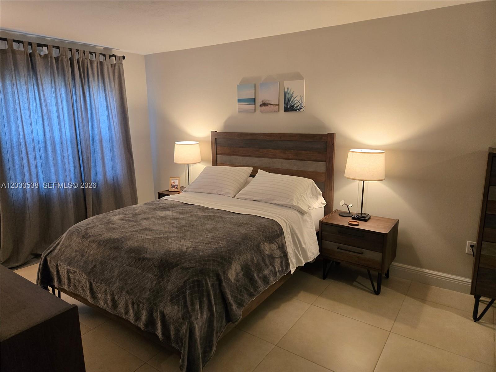 A bedroom features a wooden bed frame, two nightstands with lamps, and gray curtains — 11213 SW 88 ST # 110B, Miami FL 33176, MIAMI, FL