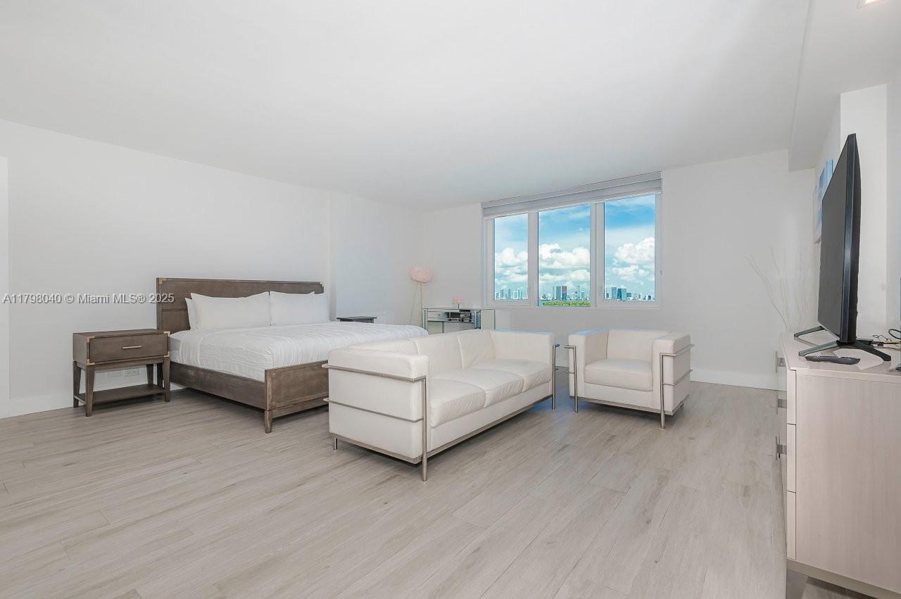 A bedroom features a bed, white sofa, armchair, and large windows with a city view — 2301 Collins Ave # 1531, Miami Beach FL 33139, MIAMI BEACH, FL