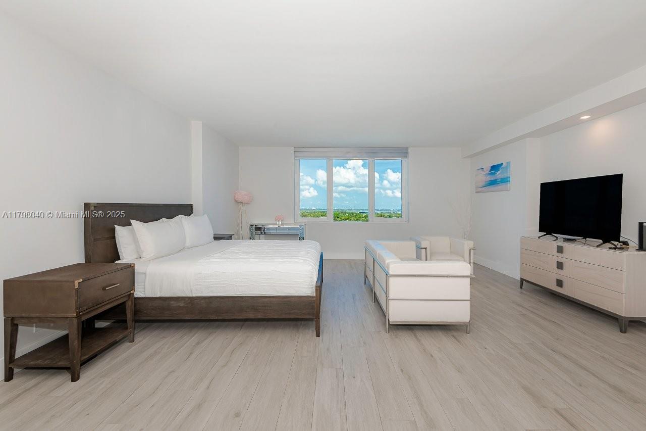 A spacious bedroom features a bed, white sofa, television console, and large windows with views — 2301 Collins Ave # 1531, Miami Beach FL 33139, MIAMI BEACH, FL