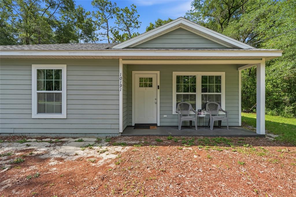 A light green house exterior features a front porch, a white door, and two chairs — 10191 NE 67TH LANE, BRONSON, FL