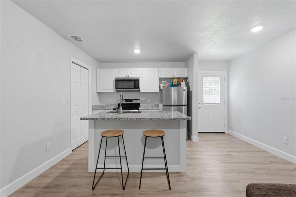 A kitchen features white cabinets, granite countertops, a center island with stools, and light flooring — 10191 NE 67TH LANE, BRONSON, FL