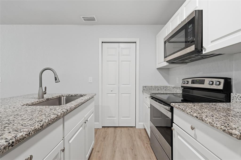 A kitchen features white cabinets, granite countertops, stainless steel appliances, and light wood-look flooring — 10191 NE 67TH LANE, BRONSON, FL