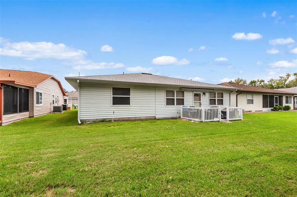 The exterior rear view of a single-story house features light siding, a small deck, and lawn — 4976 PLEASANT HOLLOW TRL, LAKELAND, FL