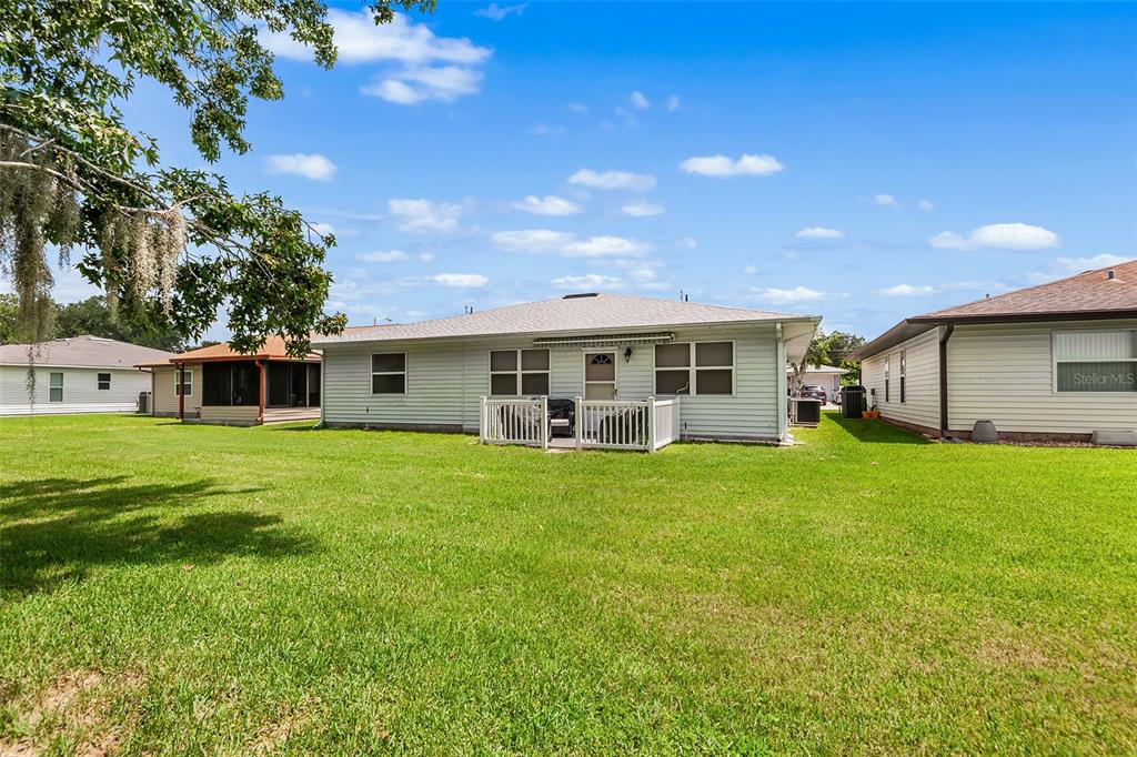 The rear exterior of a single-story house features light siding, a small deck, and lawn — 4976 PLEASANT HOLLOW TRL, LAKELAND, FL