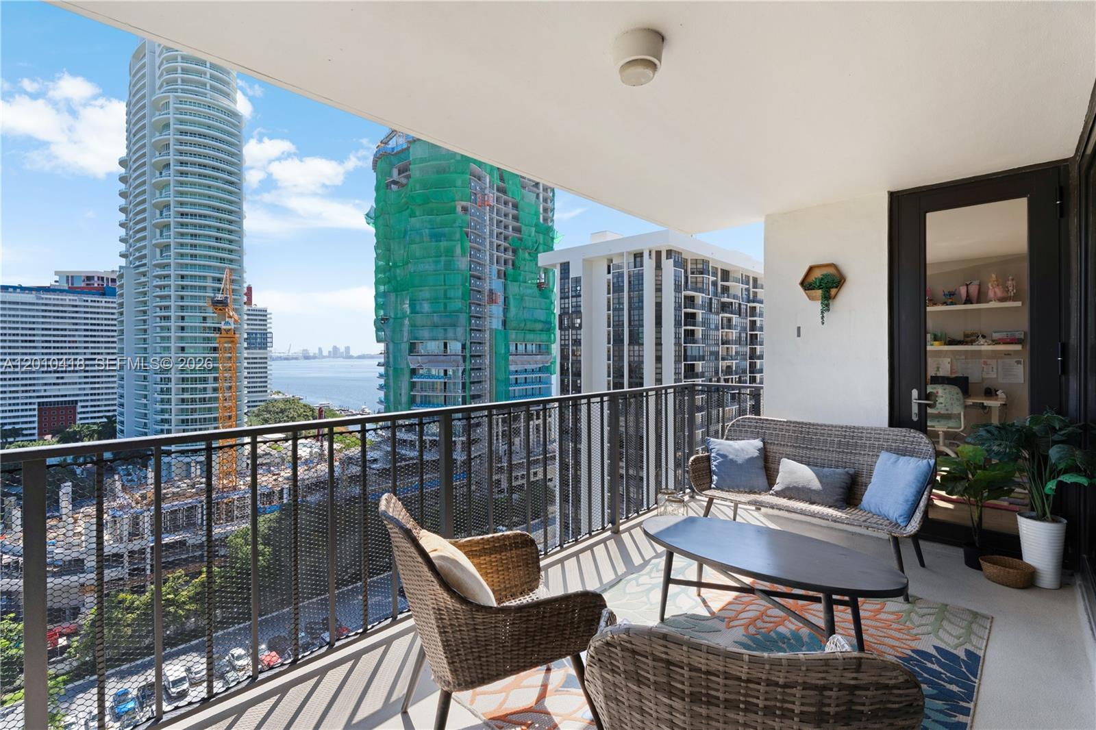 A balcony features wicker furniture, a patterned rug, and views of a bay and buildings — 1901 Brickell Ave # B1809, Miami FL 33129, MIAMI, FL