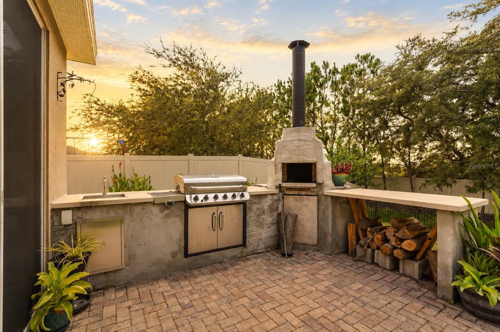 An outdoor kitchen with a grill, pizza oven, sink, and wood storage on a brick patio — 3969 ETERNITY CIRCLE, ST CLOUD, FL