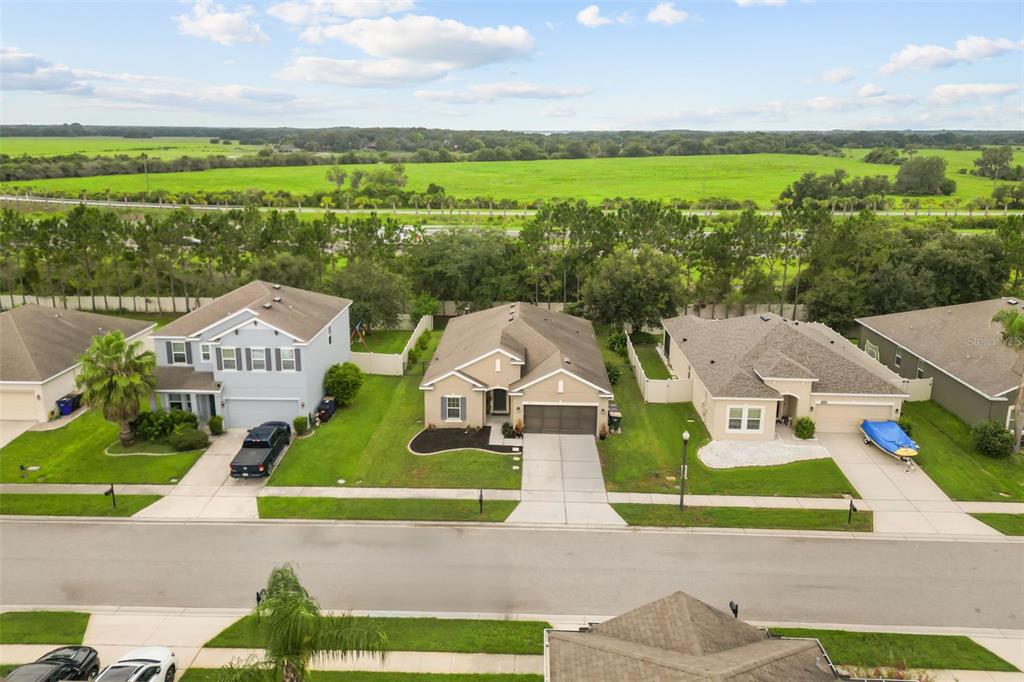 An aerial view shows three suburban houses with driveways and lawns facing a large field — 3969 ETERNITY CIRCLE, ST CLOUD, FL