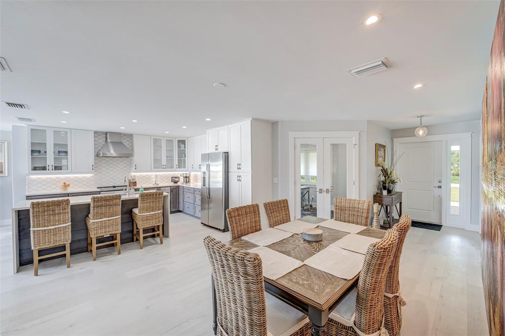 A bright open-concept kitchen and dining area featuring white cabinetry, wicker chairs, and wood flooring — 5204 TOWER DRIVE, CAPE CORAL, FL