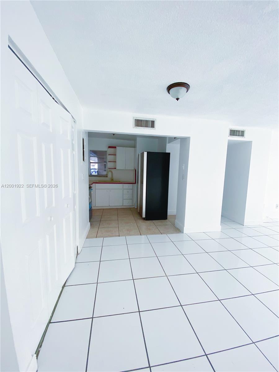 A white-tiled room leads to a kitchen featuring white cabinets and a black refrigerator — 870 NW 87th Ave # 110, Miami FL 33172, MIAMI, FL