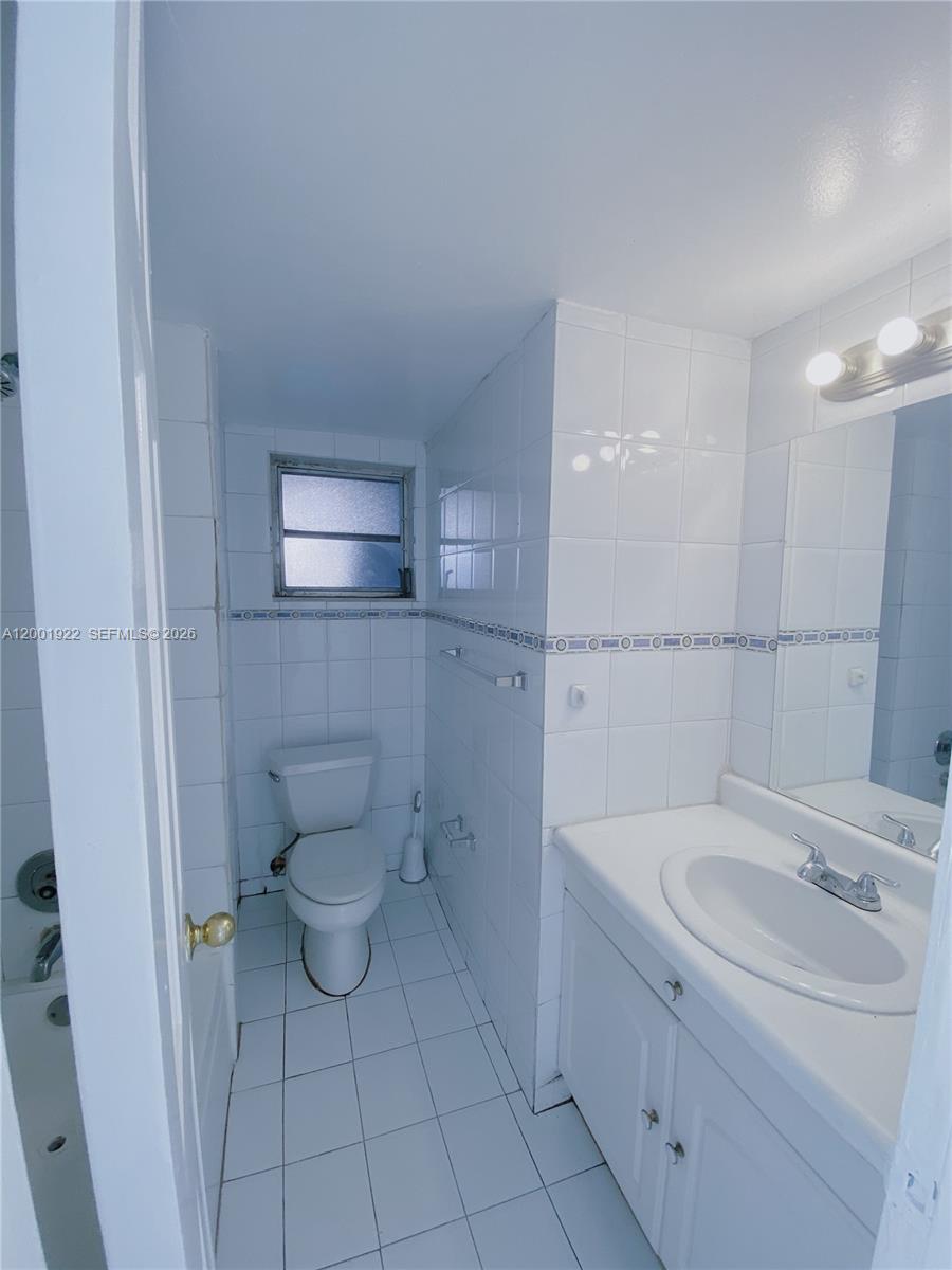 A bathroom features white tiled walls, a white vanity, and a toilet — 870 NW 87th Ave # 110, Miami FL 33172, MIAMI, FL