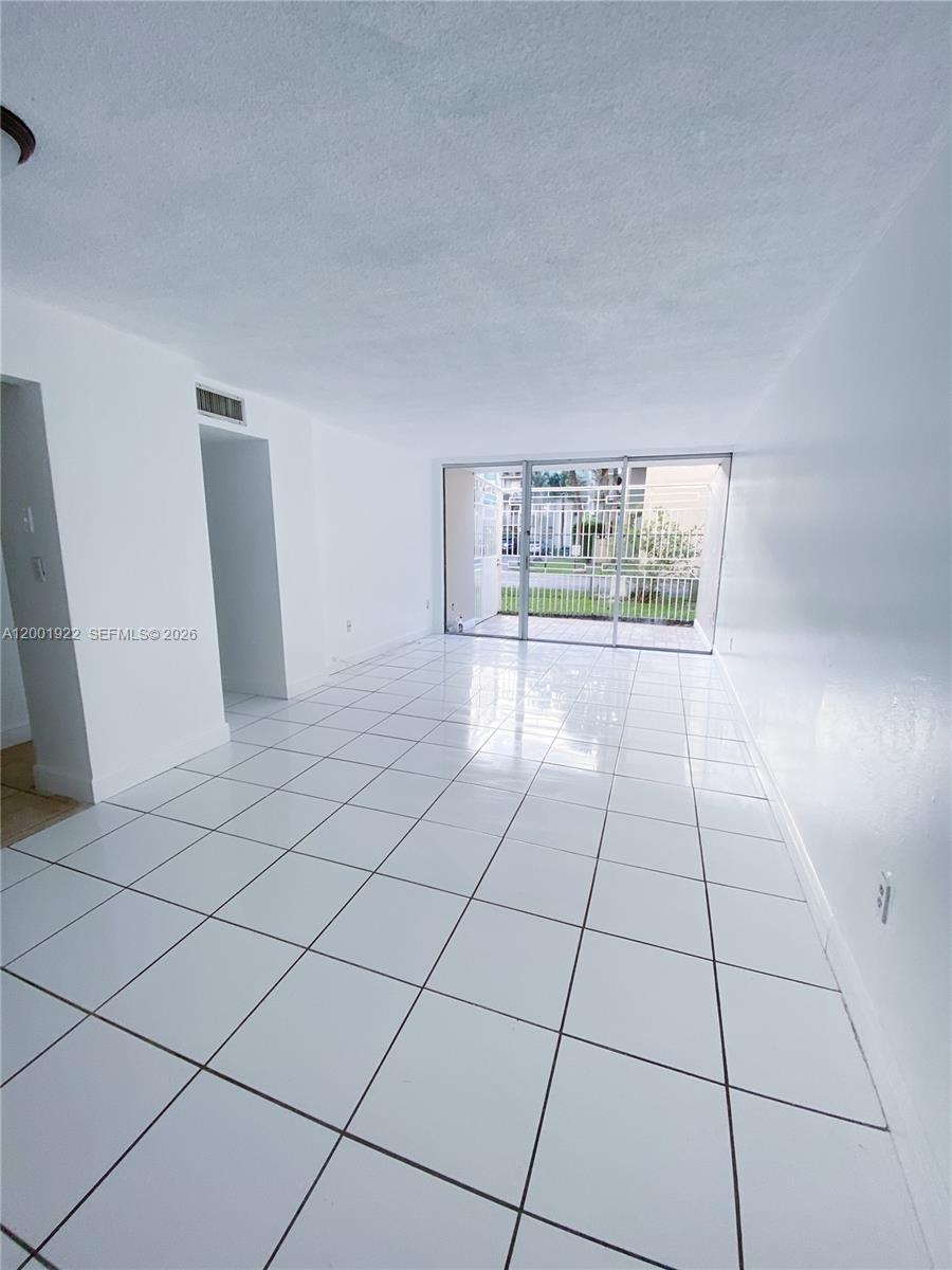 An empty room features white tiled floors, white walls, and sliding glass doors to outside — 870 NW 87th Ave # 110, Miami FL 33172, MIAMI, FL