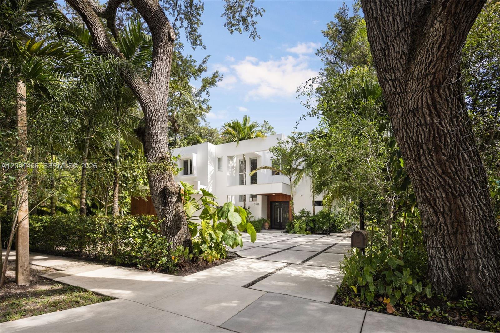A modern white two-story house is surrounded by lush trees and a paved driveway — 3901 Kumquat Ave, Miami FL 33133, MIAMI, FL